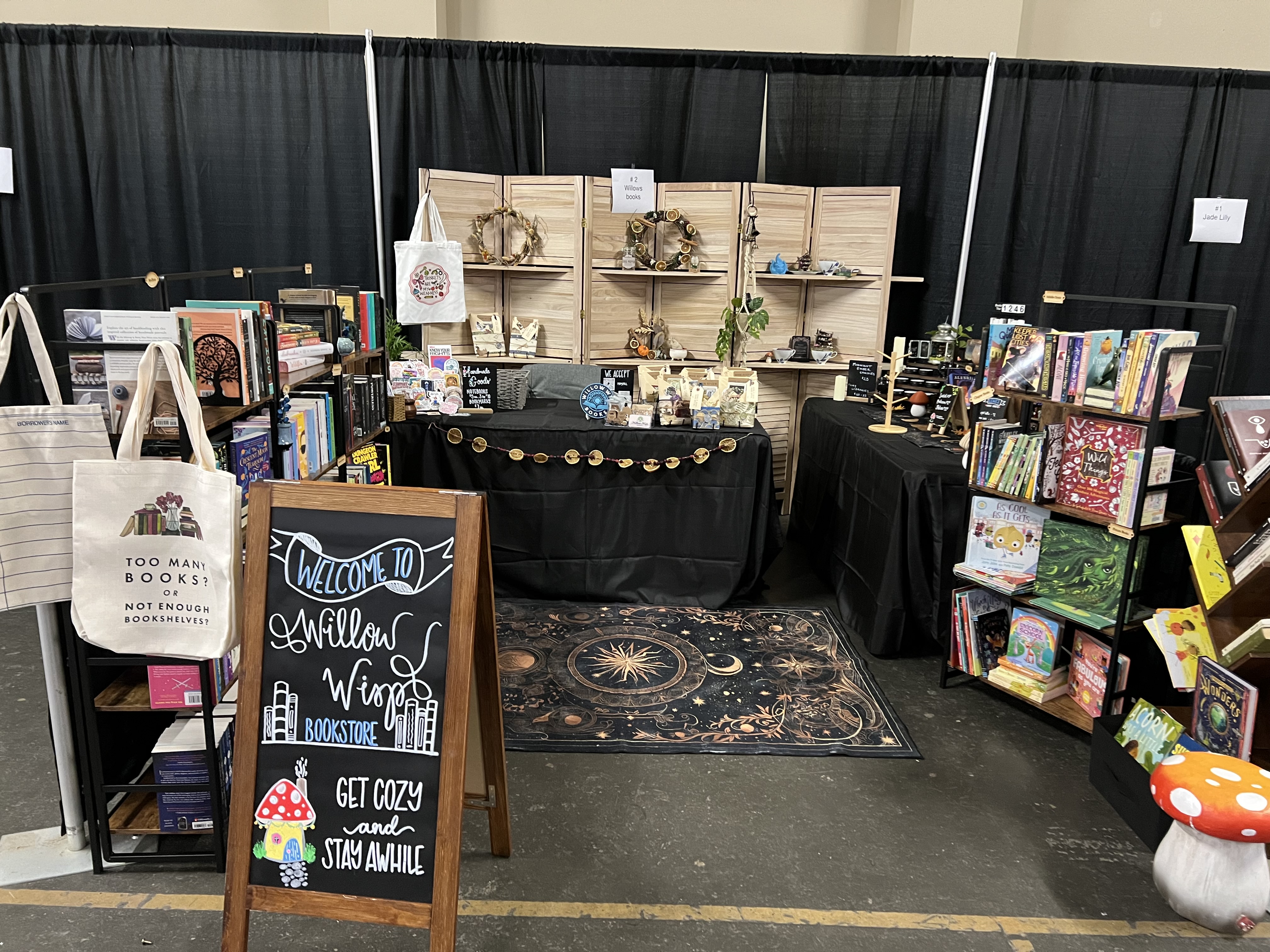Full Willow Wisp Books booth at a convention with chalkboard sign and book displays